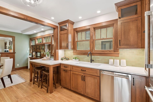 kitchen with stainless steel dishwasher, a sink, brown cabinetry, tasteful backsplash, and recessed lighting