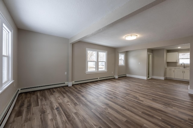 unfurnished living room with a baseboard radiator, dark wood-style floors, baseboards, and a sink