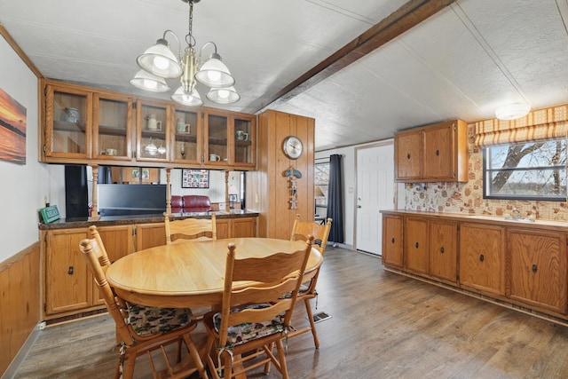 dining space featuring wood finished floors, a chandelier, beam ceiling, and a wainscoted wall