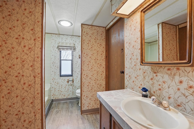 full bathroom featuring a textured ceiling, wood finished floors, toilet, and wallpapered walls