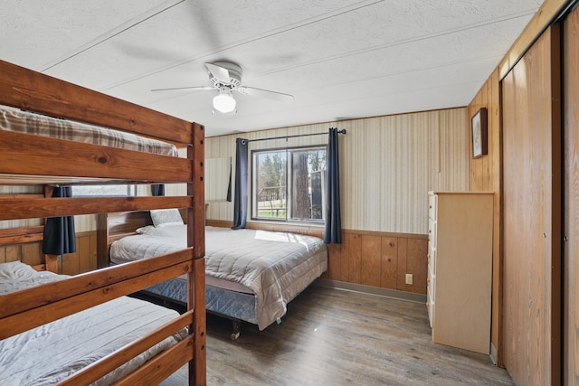 bedroom with wooden walls, ceiling fan, a wainscoted wall, baseboards, and wood finished floors