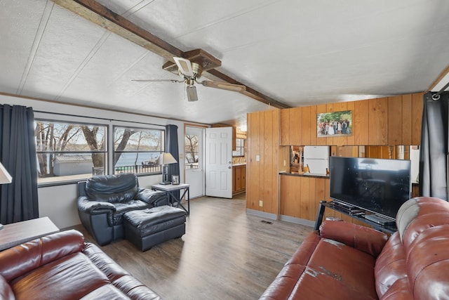 living room featuring wooden walls, vaulted ceiling with beams, a ceiling fan, and light wood-type flooring