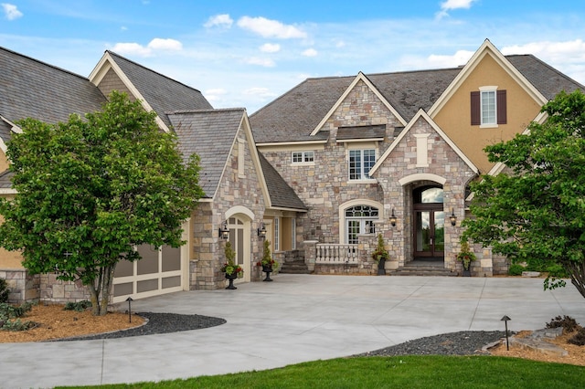 view of front of house featuring stone siding, a garage, concrete driveway, stucco siding, and french doors