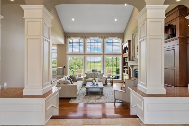 living area featuring ornate columns, a glass covered fireplace, and wood finished floors