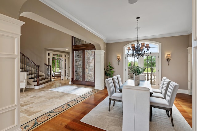 dining space with a notable chandelier, french doors, crown molding, stairs, and ornate columns