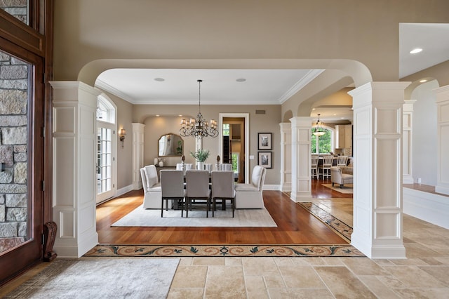 dining space featuring light wood-style floors, ornate columns, arched walkways, ornamental molding, and a notable chandelier