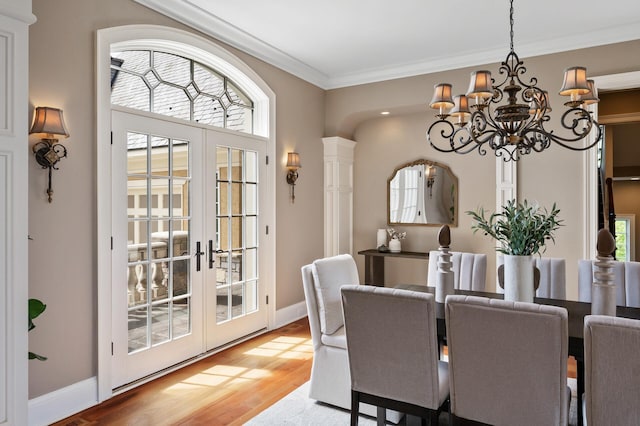 dining room featuring french doors, an inviting chandelier, ornamental molding, and light wood-style flooring