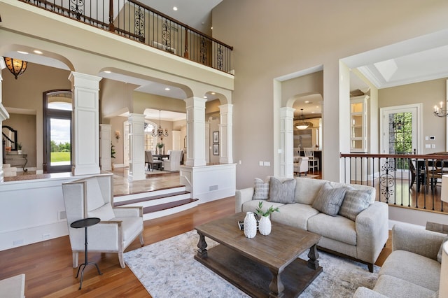 living room with decorative columns, arched walkways, a towering ceiling, a chandelier, and wood finished floors
