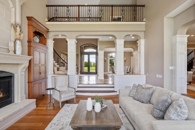 living room featuring wood finished floors, a towering ceiling, a glass covered fireplace, and stairway