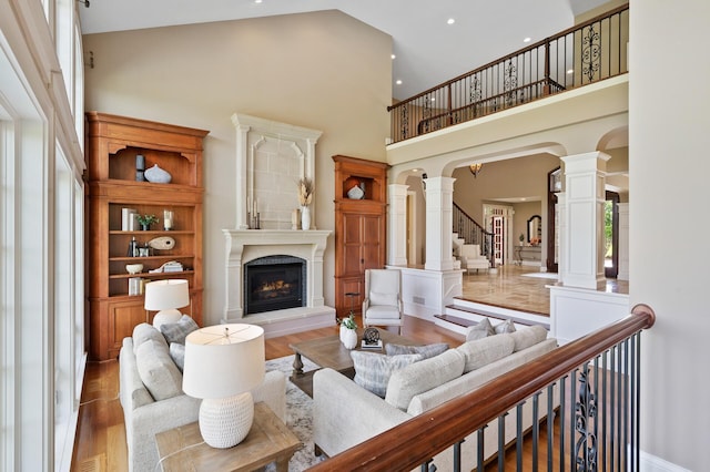 living room featuring a towering ceiling, recessed lighting, decorative columns, a high end fireplace, and wood finished floors