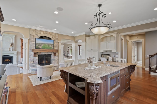 kitchen with stainless steel microwave, a fireplace, open shelves, ornate columns, and a sink