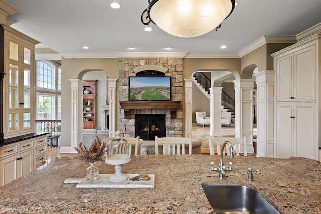 kitchen with a fireplace, arched walkways, ornate columns, light stone counters, and a sink
