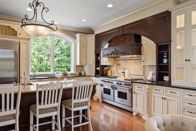 kitchen with tasteful backsplash, a sink, high end appliances, custom range hood, and cream cabinets