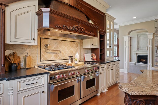 kitchen with ornamental molding, premium range hood, a fireplace, range with two ovens, and light wood-style flooring