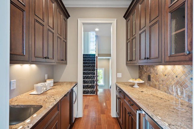 kitchen with glass insert cabinets, backsplash, light stone countertops, light wood-style floors, and a sink