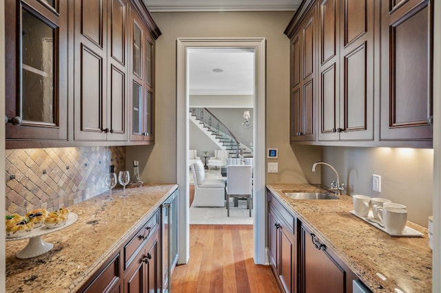 bar with tasteful backsplash, a dry bar, ornamental molding, a sink, and light wood finished floors