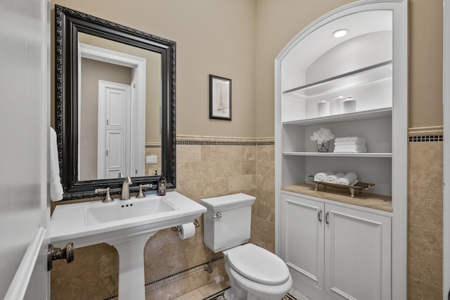 bathroom with toilet, a wainscoted wall, and tile walls