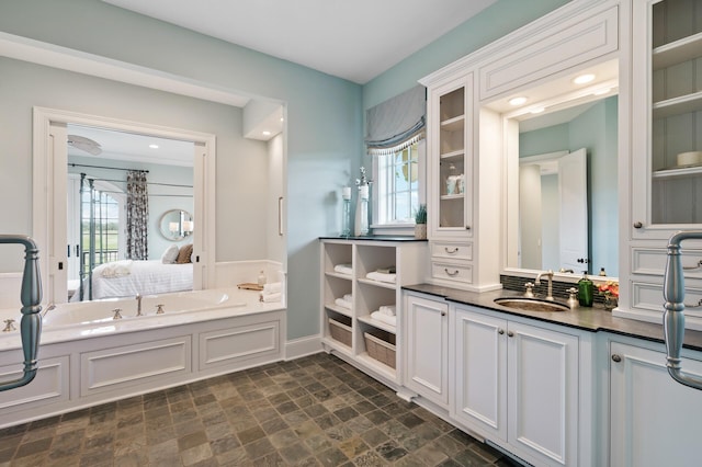 full bath with stone finish flooring, a wealth of natural light, vanity, and a garden tub