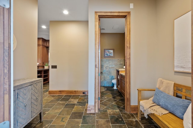 hallway featuring recessed lighting, stone finish floor, baseboards, and tile walls