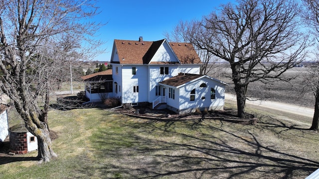 back of property with a chimney, a sunroom, a yard, and roof with shingles