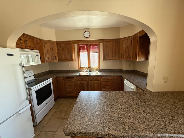 kitchen featuring a sink, dark countertops, white appliances, brown cabinetry, and light tile patterned floors