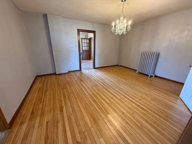 empty room with a textured ceiling, radiator, baseboards, a chandelier, and light wood-style floors