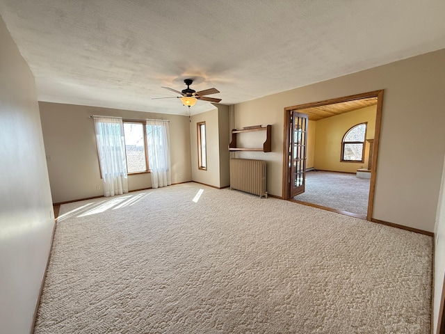 carpeted spare room with radiator heating unit, a textured ceiling, a ceiling fan, and baseboards