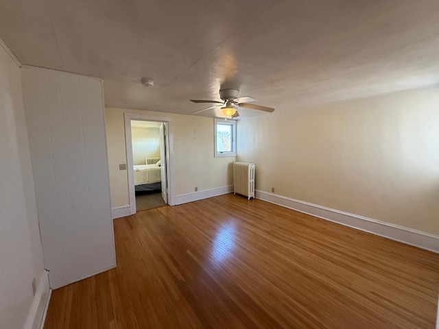 unfurnished bedroom with radiator, wood finished floors, a ceiling fan, and baseboards