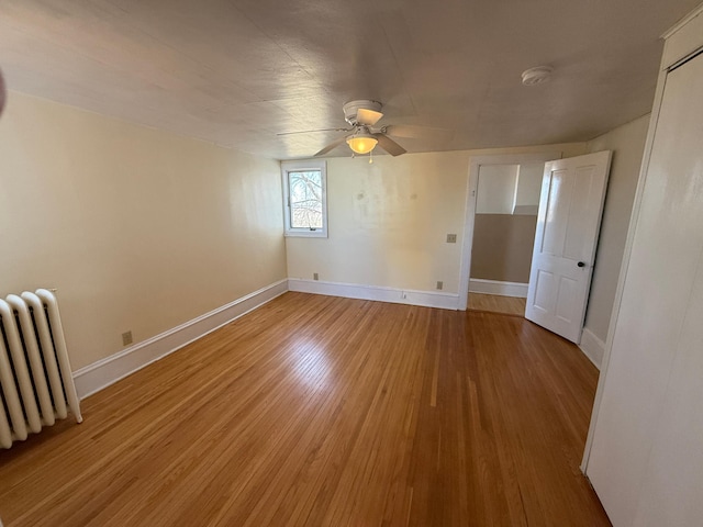 spare room with ceiling fan, baseboards, radiator heating unit, and light wood-style flooring