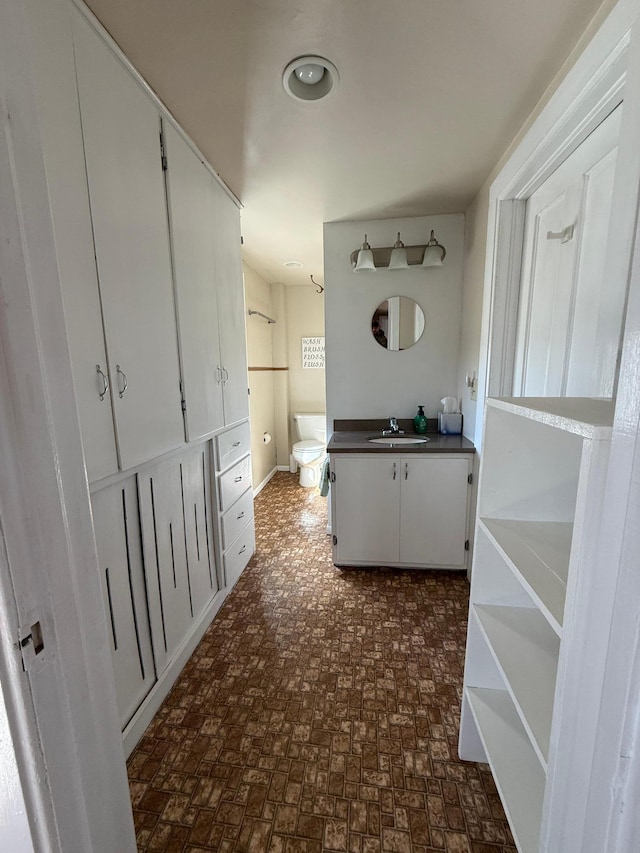 bathroom with toilet, vanity, brick patterned floor, and baseboards