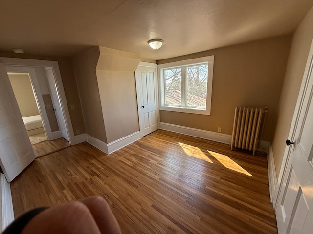unfurnished room with radiator heating unit, wood finished floors, and baseboards