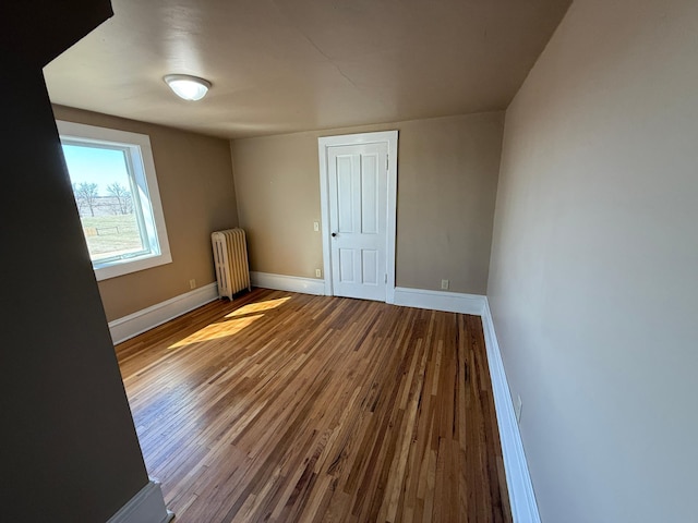 empty room with radiator heating unit, baseboards, and wood finished floors