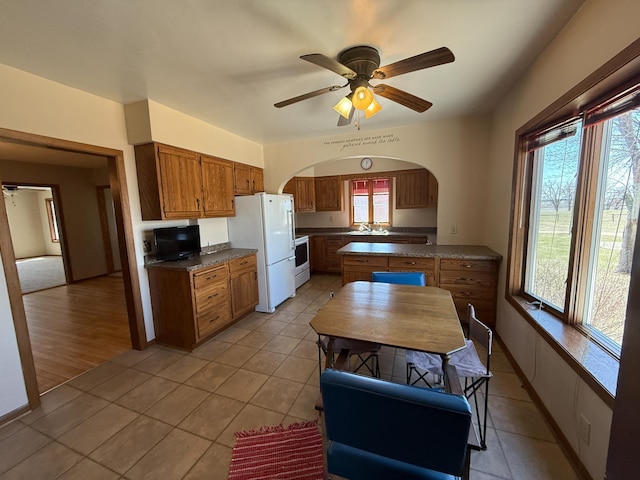 20343 680th Ave, Alden, MN 56009 - kitchen with white appliances, brown cabinetry, dark countertops, arched walkways, and light tile patterned flooring