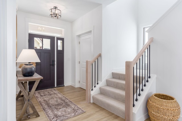 foyer entrance with stairs, light wood-style flooring, and a notable chandelier