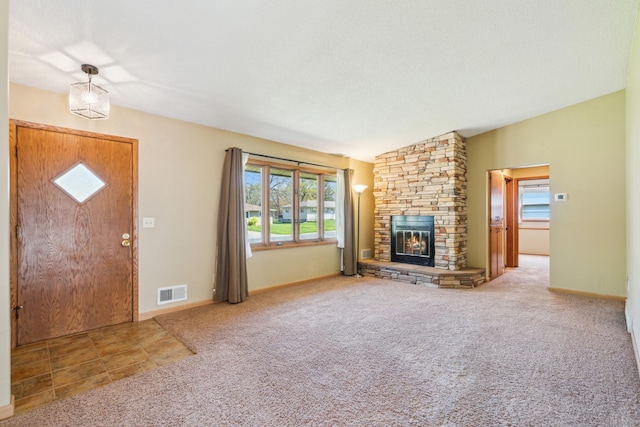 unfurnished living room with carpet flooring, a stone fireplace, and baseboards