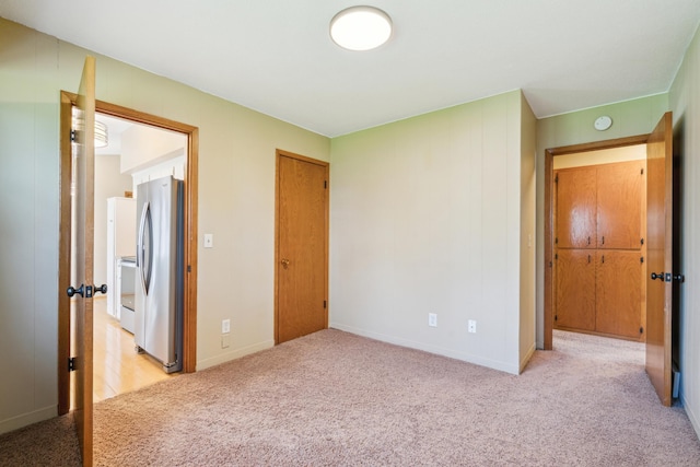 unfurnished bedroom with freestanding refrigerator, light carpet, a closet, and baseboards