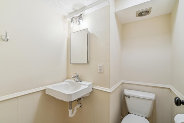 bathroom featuring toilet, a wainscoted wall, a decorative wall, and a sink