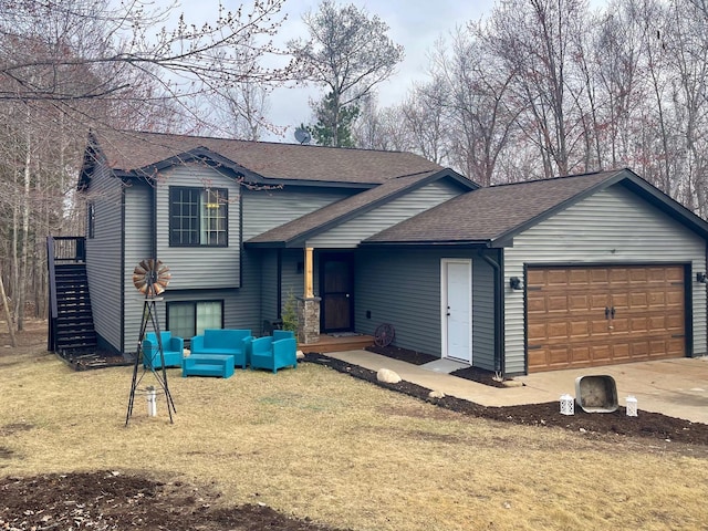 tri-level home featuring roof with shingles, an attached garage, a front yard, an outdoor living space, and driveway