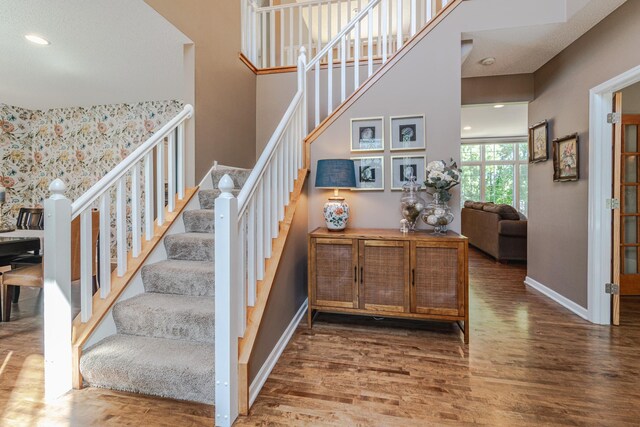 stairway with wood finished floors, baseboards, recessed lighting, and a high ceiling