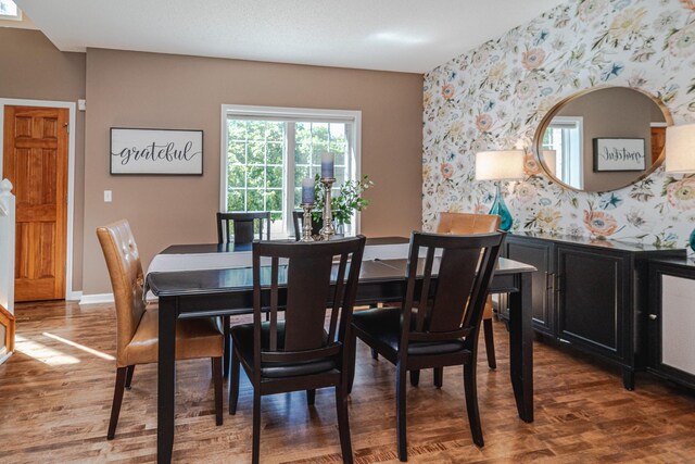 dining space with wallpapered walls, wood finished floors, baseboards, and an accent wall