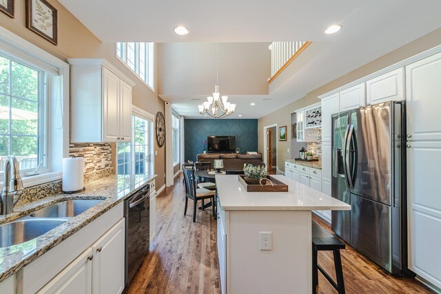 kitchen with stainless steel fridge, a sink, plenty of natural light, black dishwasher, and a high ceiling