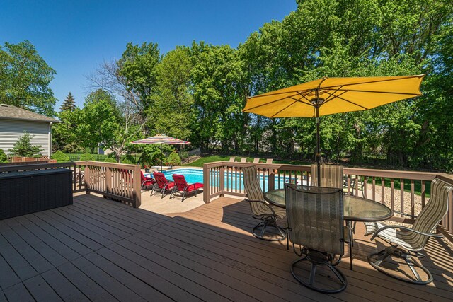 wooden deck with outdoor dining area, an outdoor pool, and view of wooded area