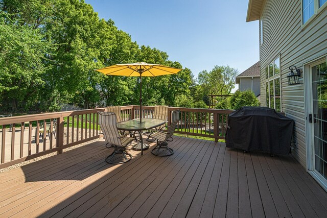 wooden terrace with area for grilling, outdoor dining space, and view of scattered trees