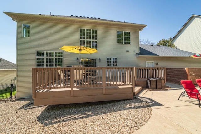 rear view of house with fence, a deck, a patio area, and roof with shingles