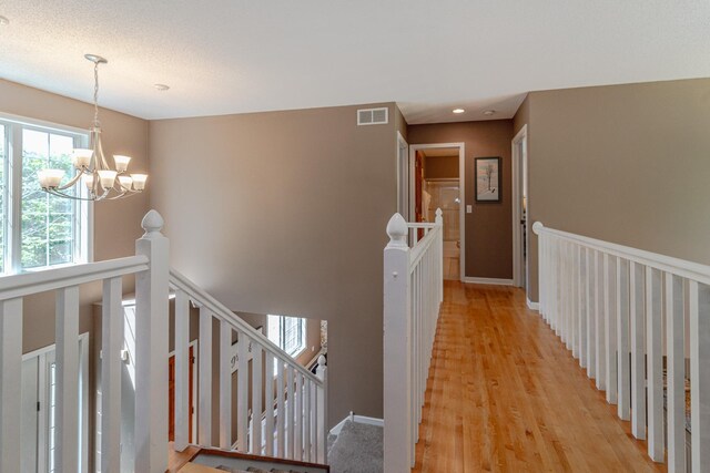 corridor featuring an upstairs landing, light wood-style flooring, a chandelier, and baseboards