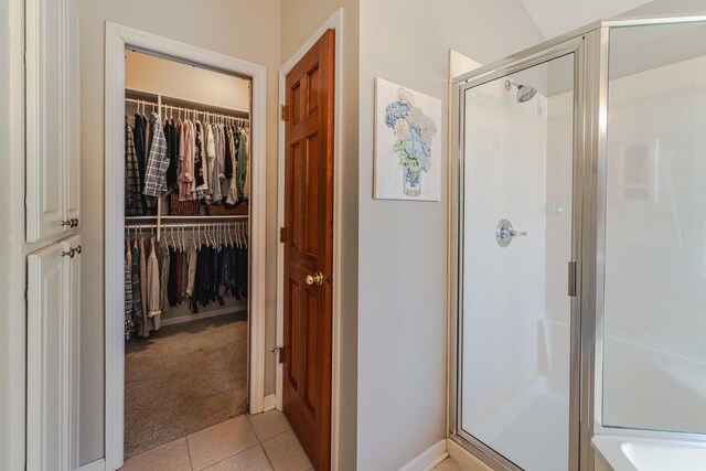 bathroom with a stall shower, tile patterned flooring, a walk in closet, and baseboards