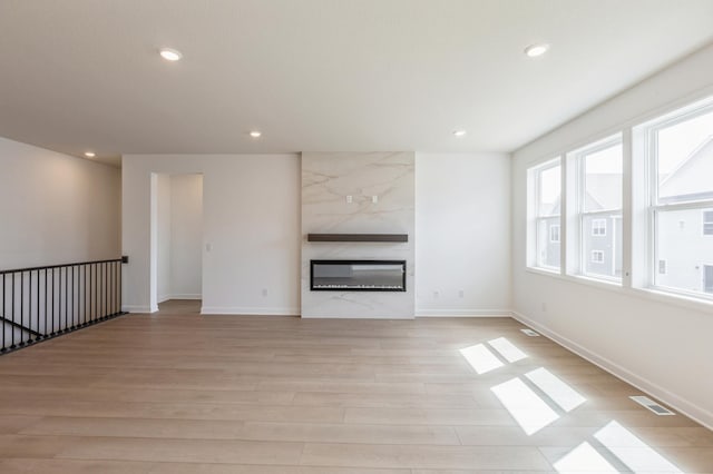 unfurnished living room featuring light wood-type flooring, a large fireplace, visible vents, recessed lighting, and baseboards