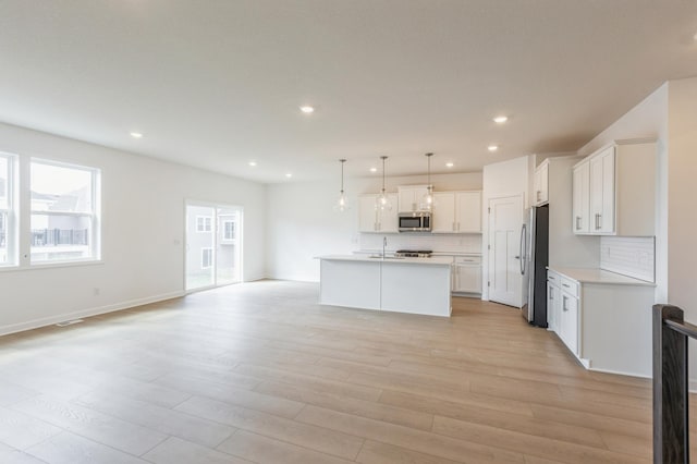 kitchen featuring tasteful backsplash, open floor plan, light countertops, appliances with stainless steel finishes, and light wood finished floors