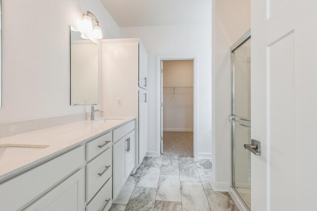 full bathroom with a sink, a stall shower, a walk in closet, marble finish floor, and double vanity