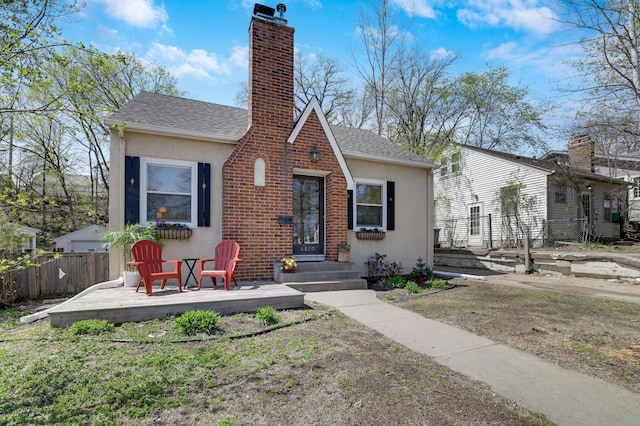 view of front facade with fence, stucco siding, a chimney, and a deck